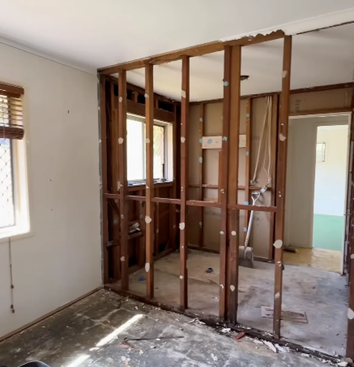 A room in an older home with one wall stripped to the timber studs and a doorway through to a green painted room.