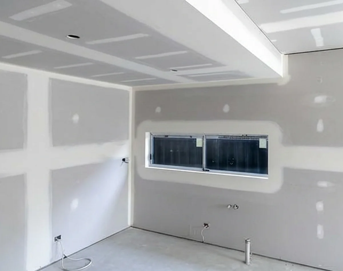 A sheeted room with a stepped bulkhead running around the ceiling and a small window set into the wall below it.