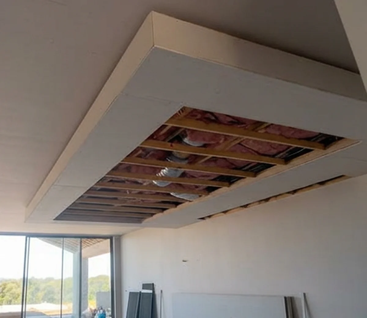 A bulkhead sheeted around an open ceiling panel, with the joists, the insulation and the light fittings still visible inside it.