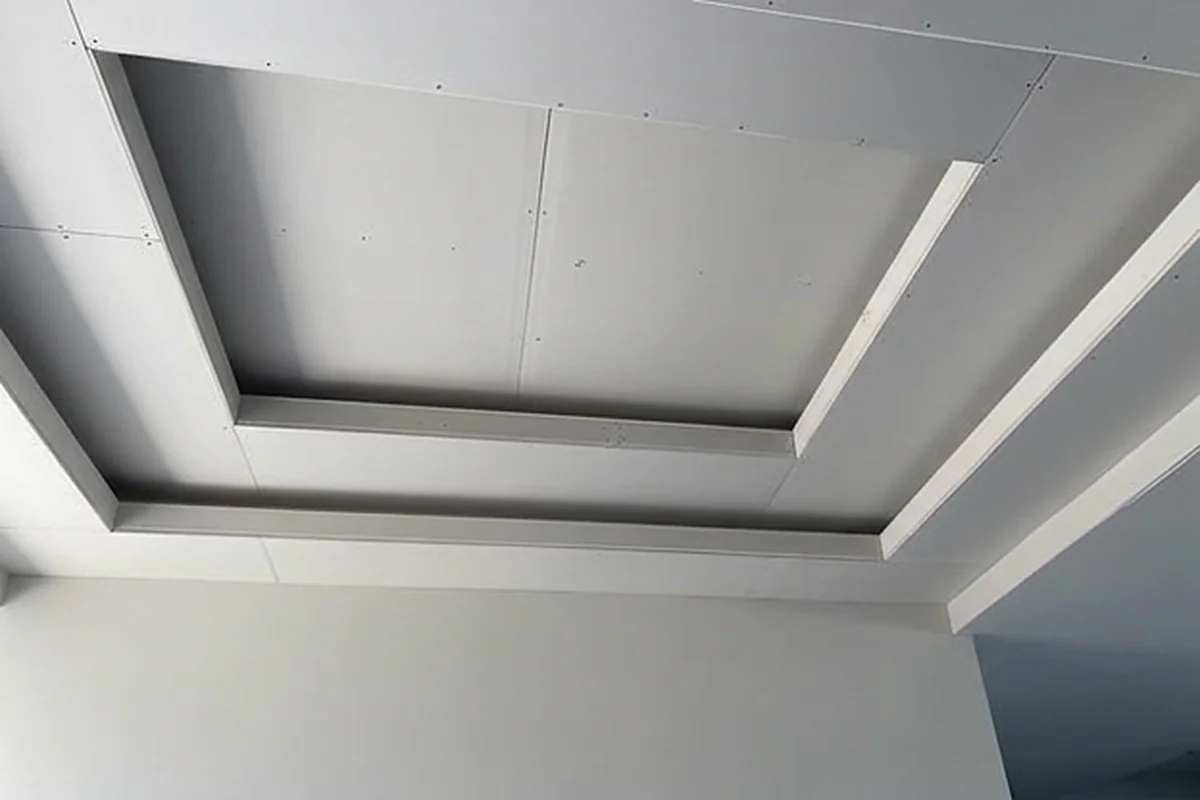 A stepped bulkhead running around a ceiling, sheeted and screwed off, with a shadow line detail along one edge.