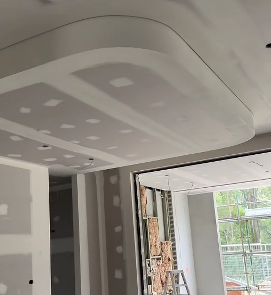 A curved bulkhead with a rounded corner set into a ceiling, sheeted and set, above a doorway looking out to the yard.