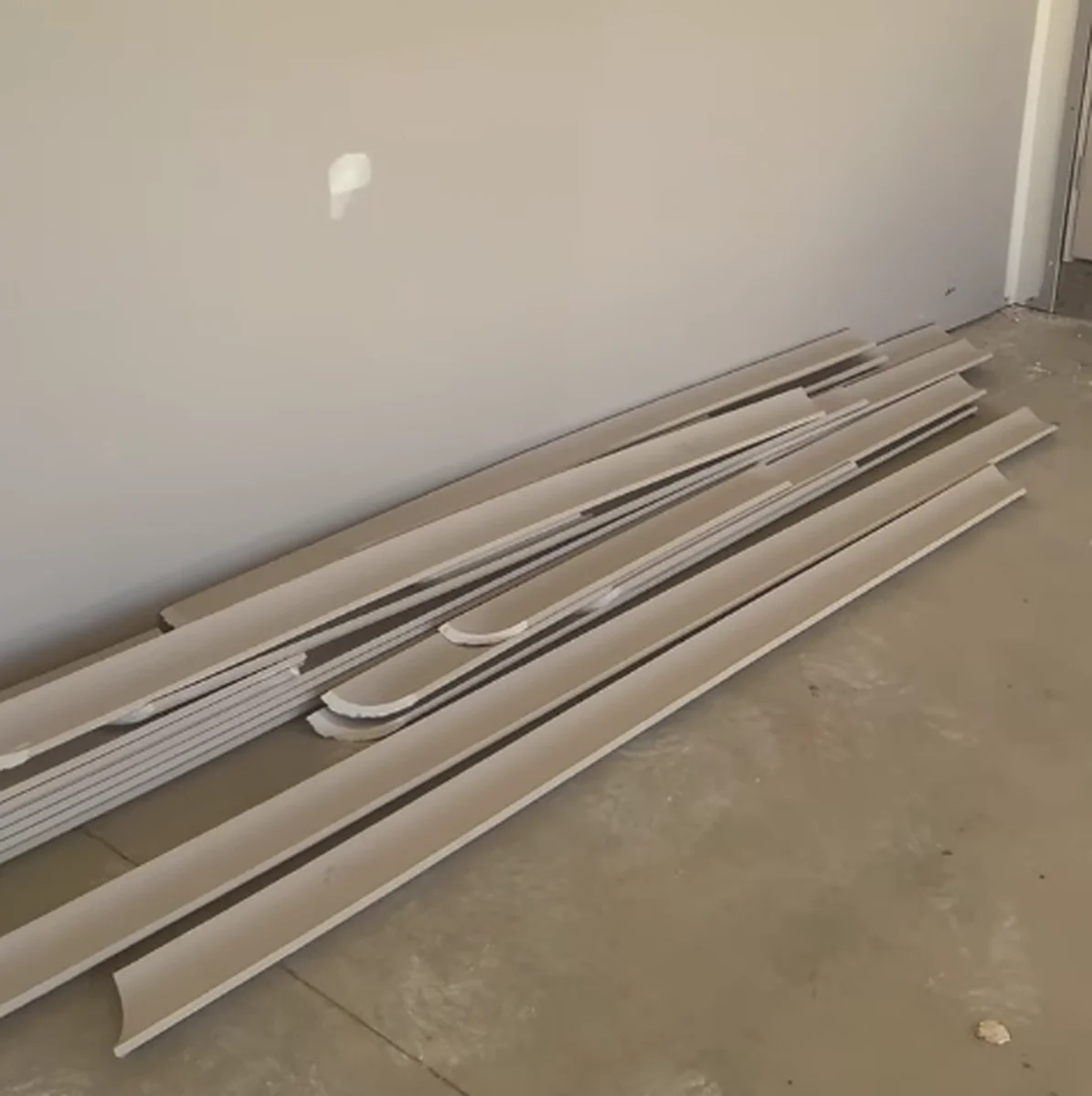 Lengths of cornice in several different profiles leaning against a wall on a tiled floor.