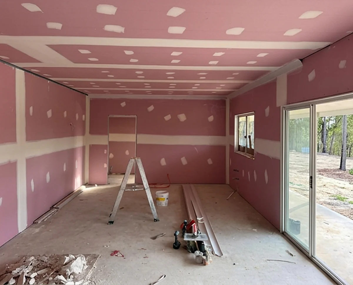 A long room lined in pink fire rated sheets with the ceiling set, a stepladder standing in it and cornice lengths on the floor.