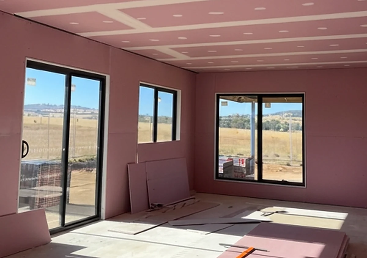 A room lined in pink fire rated plasterboard with sliding doors, and offcuts of sheet stacked on the floor.