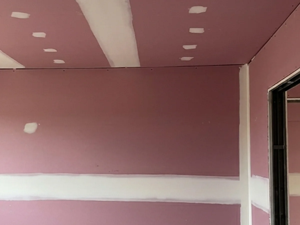 A pink fire rated wall and ceiling meeting at a set corner, with the joints run in white compound.