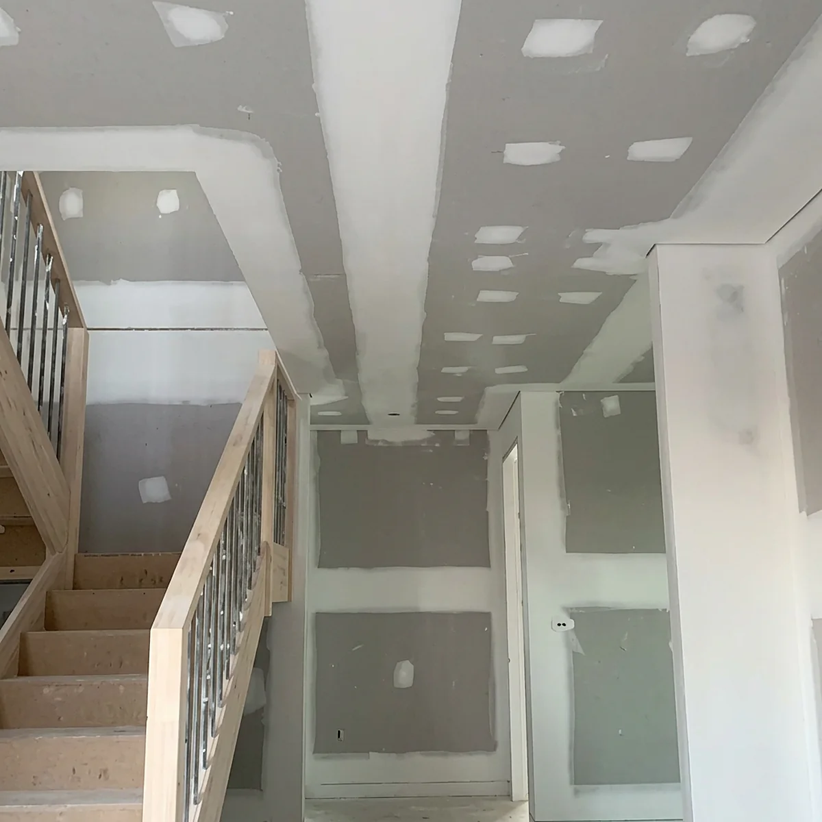A stairwell and upstairs landing lined in plasterboard, with a timber balustrade and a ceiling of set joints and spotted screw heads.