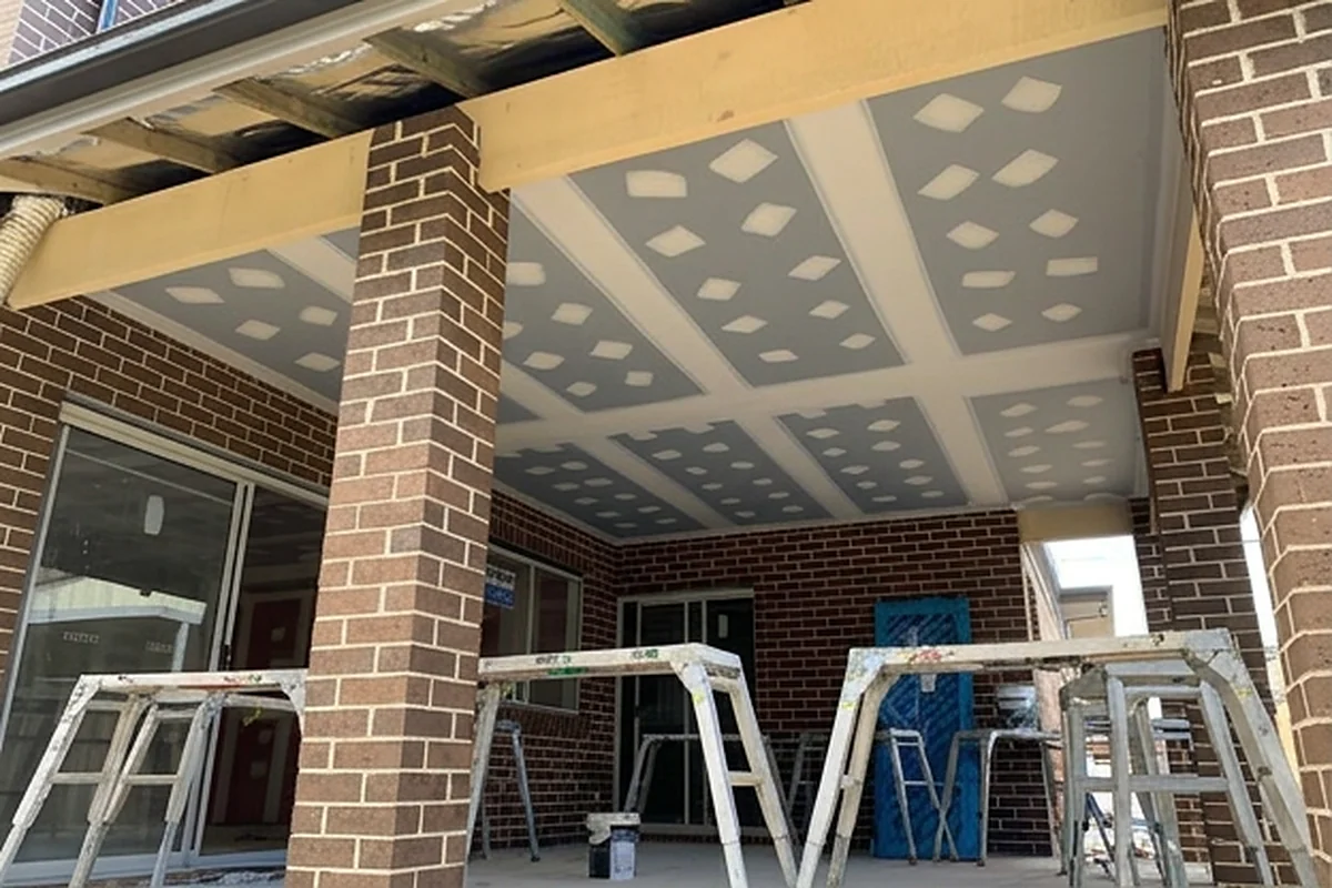 A finished patio ceiling between brick piers, sheeted and set, with trestles standing on the slab below.