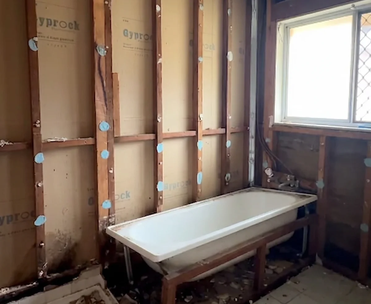 A bathroom stripped back to the framing with the old bath still in place, ready for new sheeting.