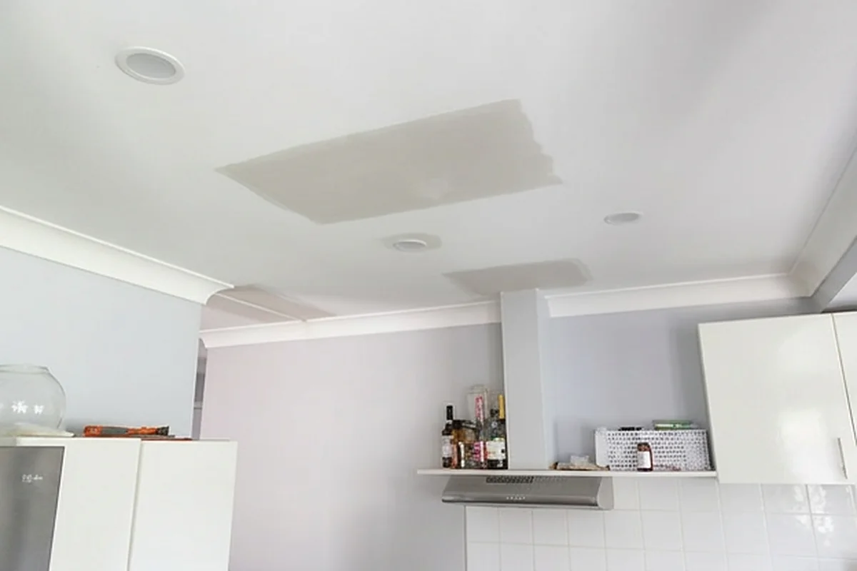 A kitchen and living ceiling with a large patch of new sheeting set into it beside the existing downlights.