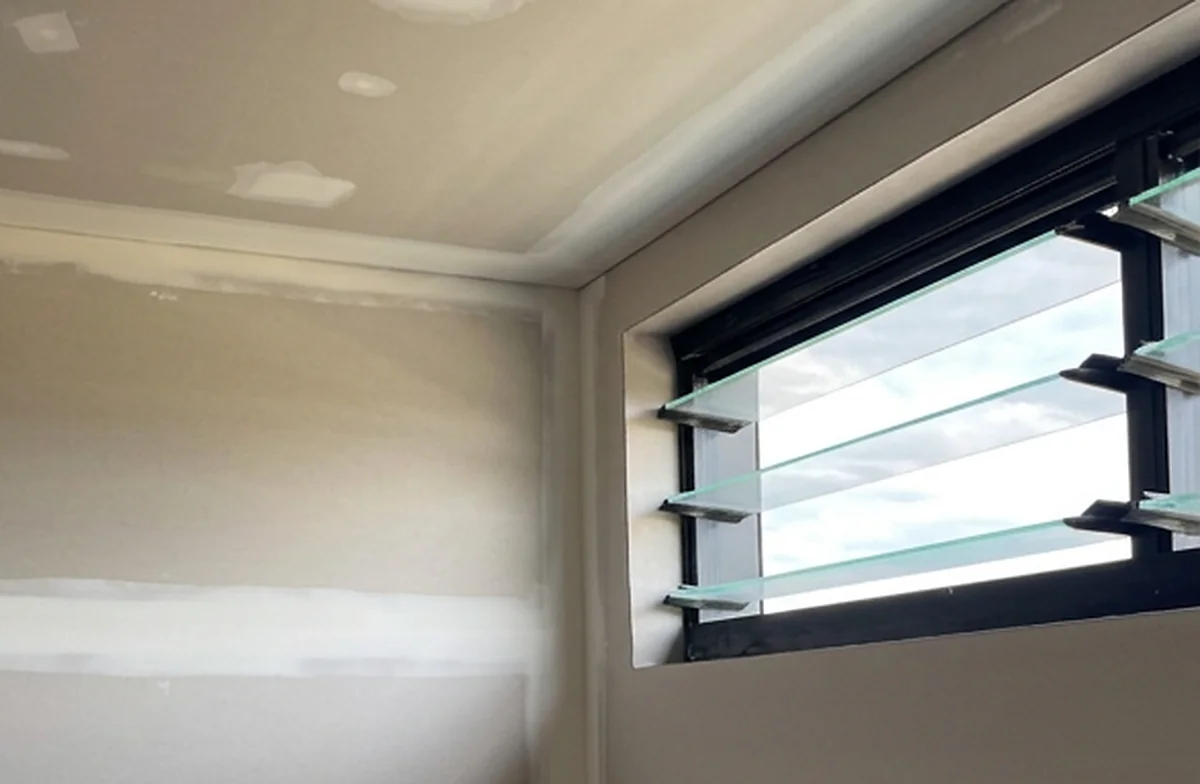 A sheeted room with a set corner and a louvre window, the joints run and the walls waiting for paint.