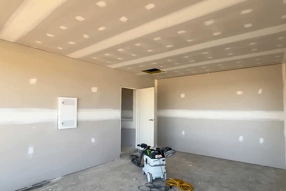 A large sheeted room with a set ceiling and a doorway through to the next room, with a dust extractor on the slab.