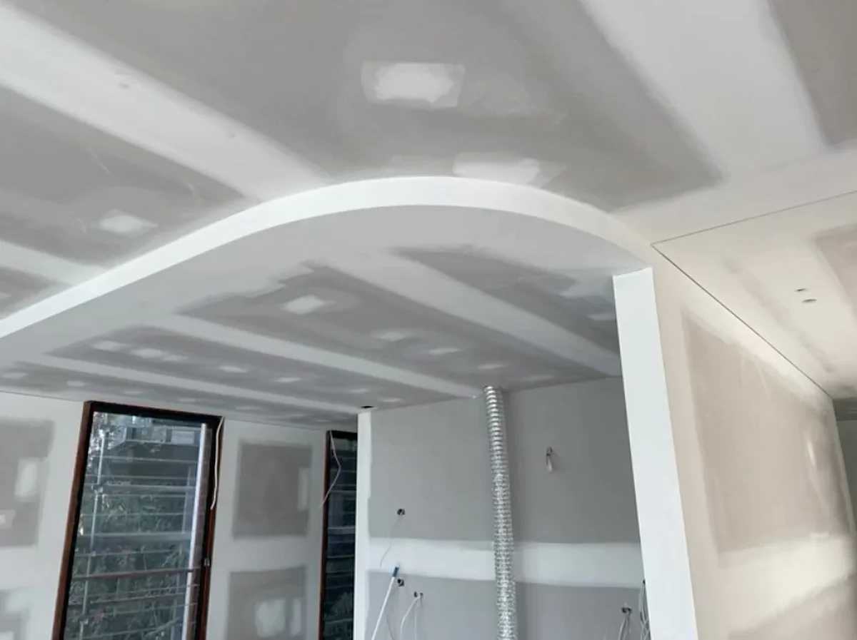 A finished ceiling with a wide curved bulkhead sweeping across the room, sheeted and set before painting.