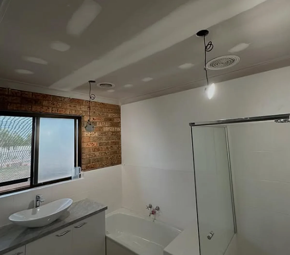 A finished bathroom with a new set ceiling, an exhaust fan and downlights, above the bath and the shower.